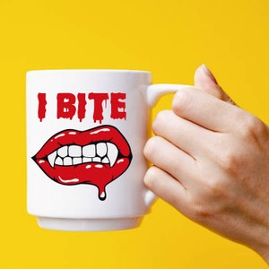 K&ouml;nnte beinhalten: Wei&szlig;e Keramik-Kaffeetasse mit einer roten und wei&szlig;en Illustration eines Vampirmundes mit Z&auml;hnen und dem Text "I Bite".