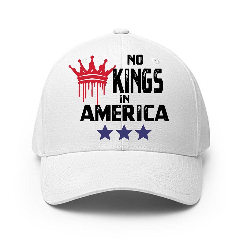 May include: White baseball cap with the text "NO KINGS IN AMERICA" in black, a red crown graphic, and three blue stars. The cap has a curved brim and a button on top.