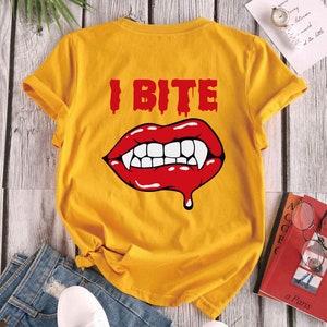 K&ouml;nnte beinhalten: Gelbes T-Shirt mit kurzen &Auml;rmeln, einem roten Vampir-Mund-Motiv und dem Text "I BITE" in Rot.