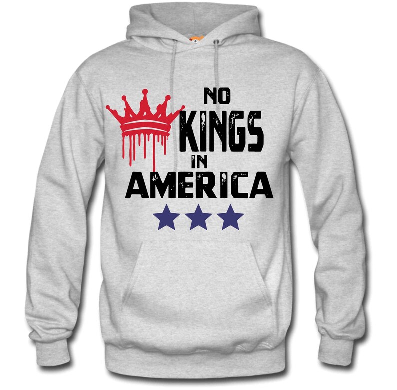 May include: A light gray hoodie with a front pocket and a hood. The front of the hoodie features the text "NO KINGS IN AMERICA" with a red crown graphic and three blue stars.