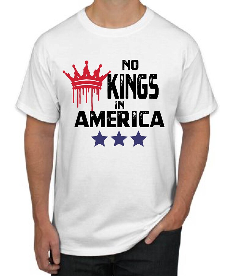 May include: White t-shirt with the text "NO KINGS IN AMERICA" in black, with a red crown graphic above. Three blue stars are below the text. The shirt is a crew neck.
