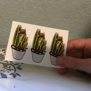 May include: Three sticker sheets with a design of a snake wearing a cowboy hat in a potted plant. The snake is brown and the plant is green and yellow.