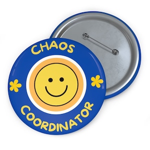 以下が含まれることがあります： 中央に笑顔の黄色い顔と「CHAOS COORDINATOR」という文字が書かれた青と黄色のボタン。ボタンの裏側は銀色です。