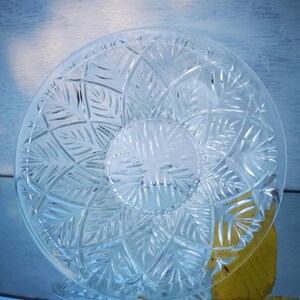 May include: A clear glass bowl with a decorative cut-glass pattern. The bowl is round and has a wide, shallow base.