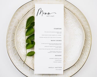 Puede incluir: Una tarjeta de menú de boda blanca con un título escrito a mano en negro "Menu Let's Eat!" y una lista de opciones de entrantes, platos principales y postres. La tarjeta está colocada encima de dos platos blancos con un borde dorado y un patrón de pequeños triángulos.