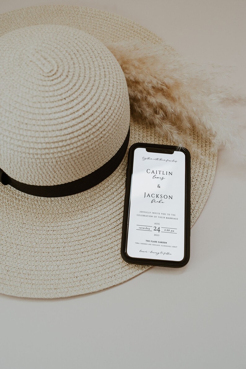 May include: A white smartphone with a black case displays a wedding invitation for Caitlin Lewis and Jackson Bole. The invitation is for Saturday, August 24th, 2023 at 4:00 PM at The Flare Garden. The phone is lying on top of a straw hat.