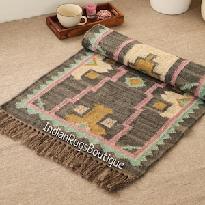 Könnte beinhalten: Ein handgewebter Teppich in Grau und Beige mit geometrischen Mustern in Rosa, Gelb und Blau. Der Teppich hat an allen Seiten Fransen und ist aufgerollt. Der Text "Indian Rugs Boutique" ist auf dem Teppich sichtbar.
