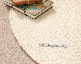 May include: A cream-colored, round jute rug with a woven texture. Two vintage-style journals with leather covers and map designs are on the rug. The text "IndianRugsBoutique" is visible on the rug.