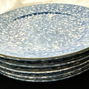 May include: A stack of five round plates featuring a blue and white speckled pattern. Each plate has a smooth, circular surface with a slightly raised rim and a consistent mottled design across the entire top face of the dinnerware set.
