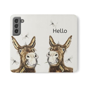 May include: A white phone case featuring a watercolor illustration of two smiling donkeys with the word "Hello". The donkeys are brown with white faces and are surrounded by dragonfly illustrations.