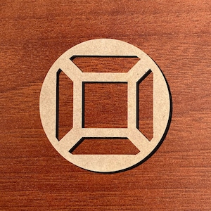 May include: A round, light brown wooden cutout with a geometric design. The design features a square within a square, connected by straight lines, all enclosed within a circle. The cutout is set against a dark brown wooden surface.