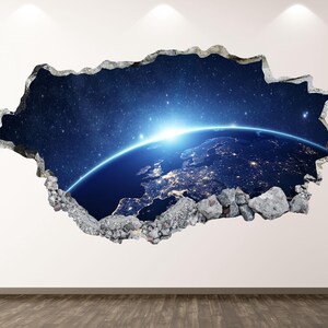 Puede incluir: Un vinilo decorativo que presenta un efecto 3D de un agujero que revela una vista de la Tierra desde el espacio. La imagen muestra el planeta con luces de ciudad, un amanecer brillante y un cielo estrellado. Los bordes del agujero son irregulares y texturizados, parecidos al hormigón roto.