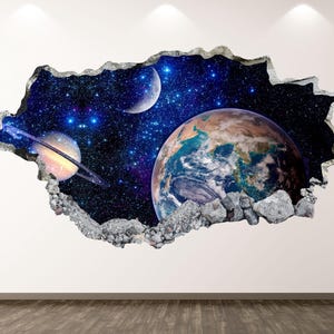 May include: A wall decal featuring a 3D effect of a hole revealing a view of space. The scene includes Earth, Saturn with rings, a crescent moon, and a starry background. The edges are framed with a gray, rocky border.