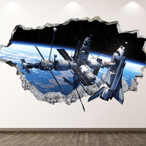 May include: A 3D wall decal showing a space station and a space shuttle against the backdrop of Earth and the starry sky. The image is designed to look like a hole in the wall, with a textured, grey border.