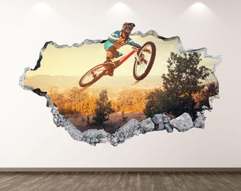 May include: A wall decal featuring a mountain biker mid-air, with a red and black bicycle. The image is framed as if breaking through the wall, revealing a landscape of trees and a sunset.