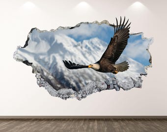 May include: A 3D wall art piece featuring a bald eagle in flight against a backdrop of snow-capped mountains and a blue sky. The eagle has brown and white feathers and a yellow beak. The artwork creates the illusion of a hole in the wall.
