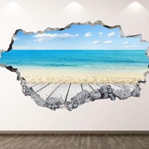 Puede incluir: Un vinilo decorativo que representa una escena de playa visible a través de un agujero en la pared. La escena incluye un océano azul, una playa de arena y un cielo azul con nubes. El borde del agujero es de piedra gris y madera.