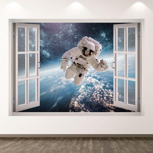 May include: A wall decal featuring an astronaut floating in space, viewed through an open window. The astronaut is wearing a white spacesuit. The window frame is white, and the background shows Earth and the starry sky.