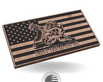 May include: Wooden American flag with a black and brown finish. The flag features the stars and stripes design, with a detailed rattlesnake and the text "DON'T TREAD ON ME". The flag is a decorative item.