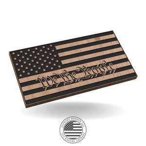 May include: Wooden American flag with laser-cut stars and stripes. The phrase "We the People" is elegantly inscribed across the stripes. The flag is a patriotic design, perfect for home decor or gifting. The logo of Patriot Design LLC is at the bottom.