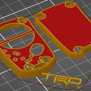 May include: 3D-printed case components in gold and red. The design includes a main body with a circular cutout and several smaller holes, and a separate lid. The word "TRD" is visible in gold.