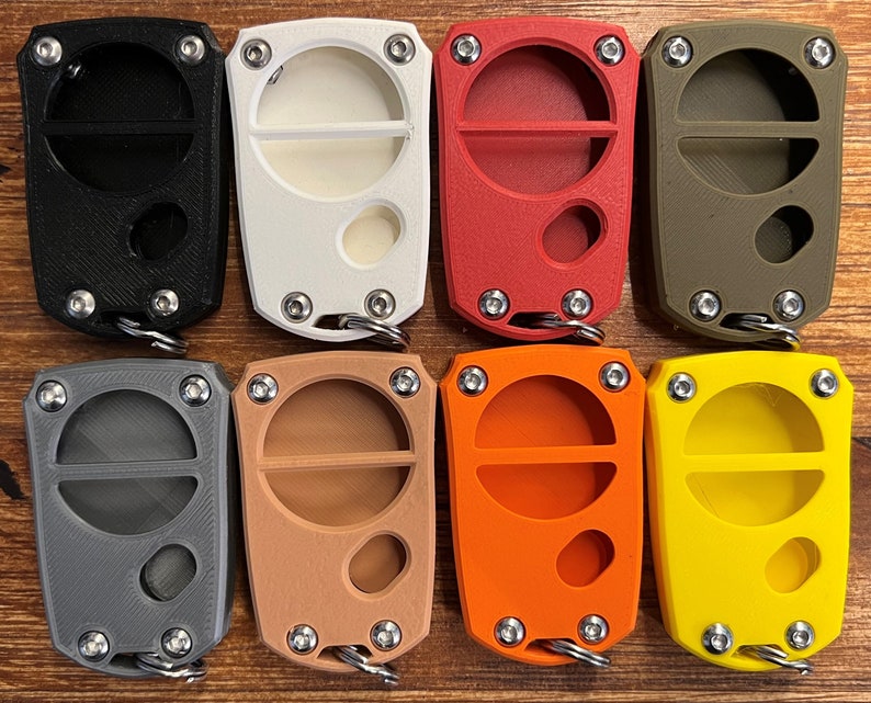 May include: Eight key fobs in a range of colours: black, white, red, olive green, grey, tan, orange, and yellow. Each fob has a rectangular form with a circular opening and a metal keyring attachment. The fobs are secured with four small screws.