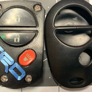 May include: Two black car key fobs. One has a blue "TRD" logo and an orange button. The other is a plain black fob. Both have buttons for locking and unlocking the car.