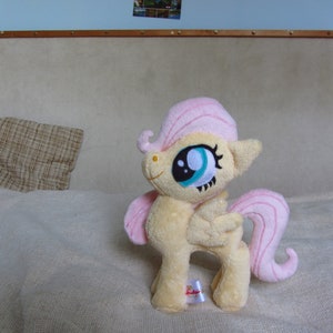 May include: A plush toy of Pinkie Pie from My Little Pony. The toy is pink and yellow with a blue eye and a pink mane.