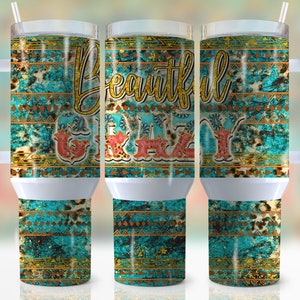 May include: White tumbler with a turquoise, gold, and brown patterned design. The tumbler has a handle and a straw. The text "Beautiful Crazy" is printed on the tumbler.