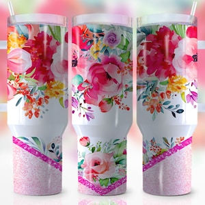 May include: A white stainless steel tumbler with a pink glitter bottom and a floral design featuring pink, yellow, and blue watercolor flowers. The tumbler has a white handle and a straw.