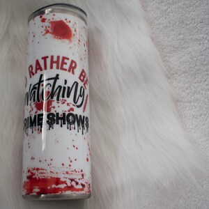 May include: White stainless steel tumbler with a red splatter design and the text "I'd rather be watching crime shows".