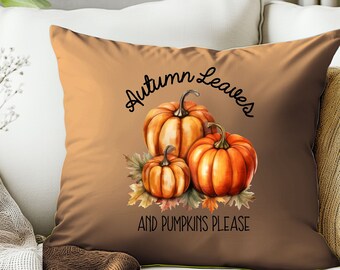 May include: A square throw pillow with a gradient brown background featuring a central illustration of three orange pumpkins resting on colorful autumn leaves. The text "Autumn Leaves" is printed in black above and "AND PUMPKINS PLEASE" below.