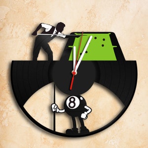 Könnte beinhalten: Eine schwarze Schallplattenuhr mit einem grünen Filz-Billardtisch und einer Cartoon-8-Ball, die einen Queue hält. Die Uhrzeiger sind rot und weiß.