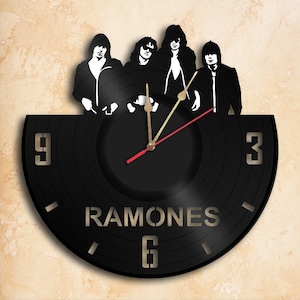 May include: A black vinyl record clock featuring a silhouette of the Ramones band members. The clock face has Roman numerals and the band's name is printed in white.