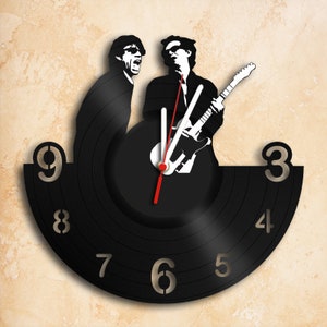 Könnte beinhalten: Eine schwarze Schallplattenuhr mit einer Silhouette von zwei Musikern, einer spielt Gitarre. Das Zifferblatt der Uhr hat weiße Zahlen und einen roten und weißen Uhrzeiger.