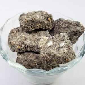 May include: A glass bowl filled with grey and black rock-like incense pieces.