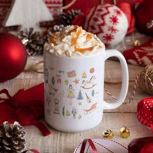 May include: White ceramic mug with a festive Christmas design featuring a nutcracker, a rocking horse, a Christmas tree, and other holiday icons. The mug is filled with a creamy beverage topped with whipped cream and caramel sauce.