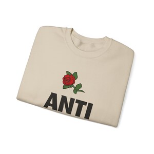 May include: A beige t-shirt with a red rose and the word "ANTI" printed in black.