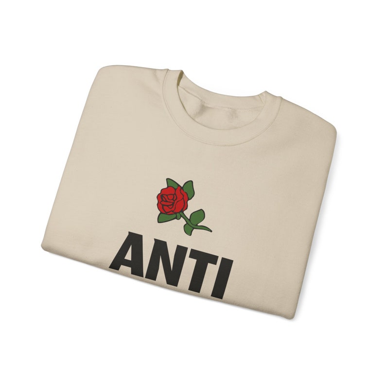 May include: A beige t-shirt with a red rose and the word "ANTI" printed in black.