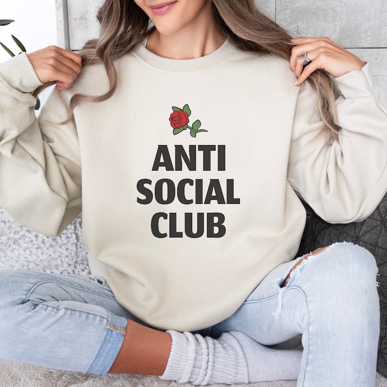 May include: A cream colored sweatshirt with the text "ANTI SOCIAL CLUB" in black letters and a small red rose graphic above the text.