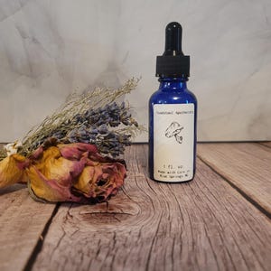 May include: A small blue glass bottle with a dropper top. The bottle is labeled "Tawnstool Apothecary" and contains 1 fl. oz. of liquid. The label also includes a mushroom illustration and the text "Made with care in Blue Springs, MO".