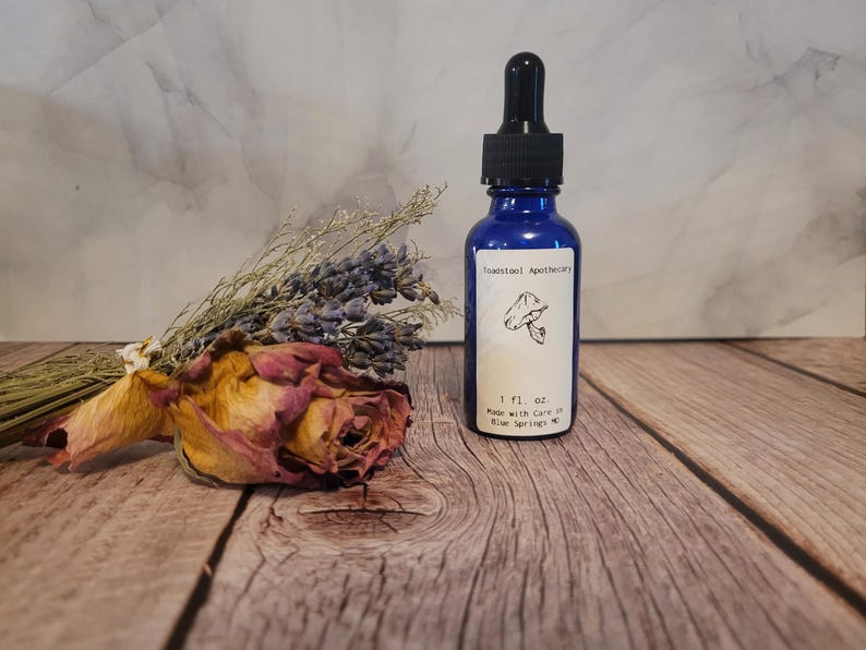 May include: A small blue glass bottle with a dropper top. The bottle is labeled "Tawnstool Apothecary" and contains 1 fl. oz. of liquid. The label also includes a mushroom illustration and the text "Made with care in Blue Springs, MO".