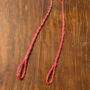 May include: Two red braided bowstrings for archery. The bowstrings are made of a durable material and are designed to be strong and reliable.
