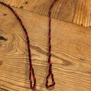May include: Two pieces of red and black braided string with loops at the ends.