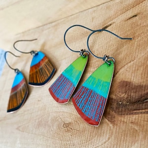 May include: A pair of handmade earrings with a geometric design. The earrings are made of metal and have a blue, green, and brown enamel finish.