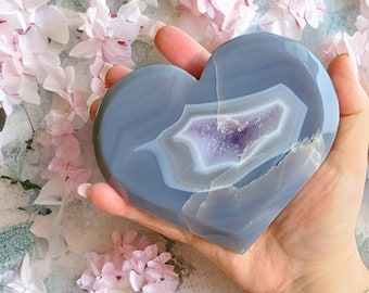May include: A heart-shaped agate crystal with a purple and white agate pattern. The crystal is a light gray color and has a smooth, polished surface.