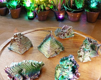 May include: A collection of six iridescent bismuth crystals in various shapes, including pyramids and clusters, displayed on a wooden surface.