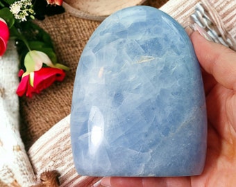 May include: A smooth, light blue, polished, oval-shaped Celestite crystal. The crystal has a cloudy, translucent appearance.