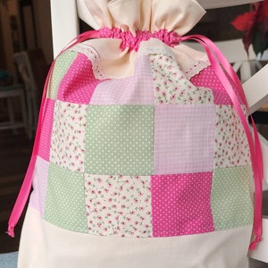 May include: A pink and green patchwork drawstring bag with a white lace trim and pink ribbon ties.