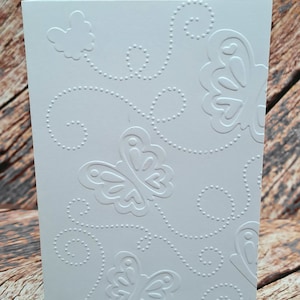 May include: White card with an embossed design of butterflies and swirls. The design is in a white-on-white pattern.